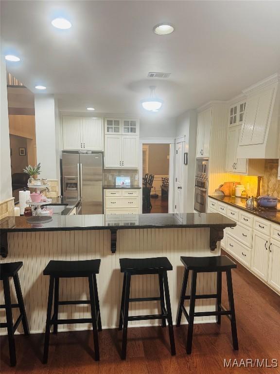 kitchen with stainless steel fridge, visible vents, decorative backsplash, dark countertops, and glass insert cabinets