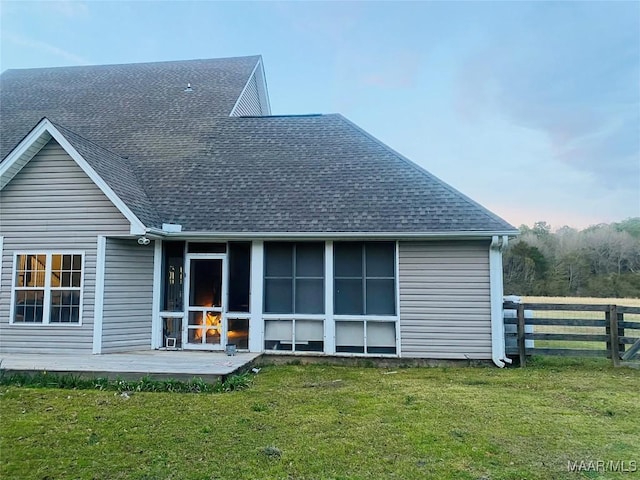 back of property featuring a sunroom, roof with shingles, a lawn, and fence