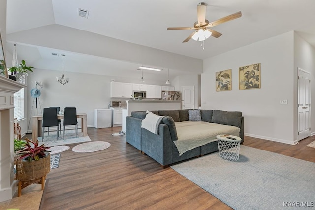 living room with visible vents, vaulted ceiling, wood finished floors, and ceiling fan with notable chandelier