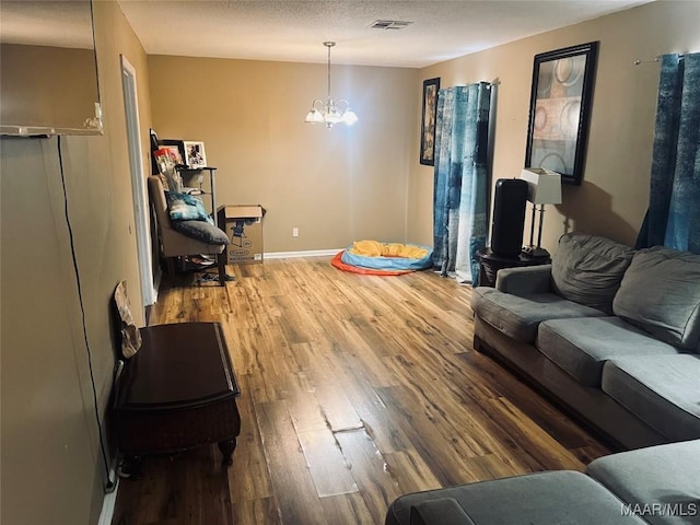 living room featuring a chandelier, a textured ceiling, wood finished floors, visible vents, and baseboards