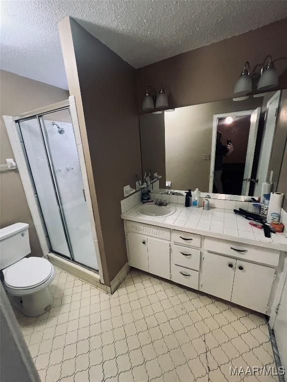 bathroom with toilet, a textured ceiling, a shower stall, vanity, and tile patterned floors