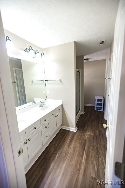 bathroom with double vanity, visible vents, a stall shower, wood finished floors, and baseboards