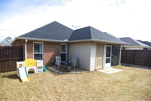 rear view of property featuring an outdoor fire pit, roof with shingles, fence, a yard, and brick siding