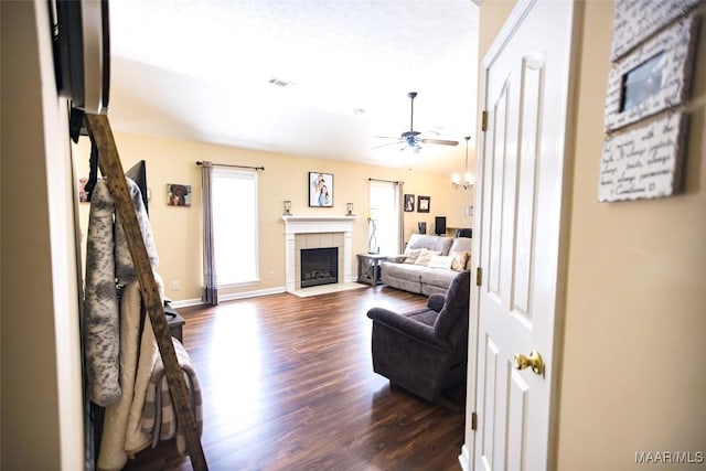 living room featuring baseboards, visible vents, a ceiling fan, a tile fireplace, and dark wood-type flooring