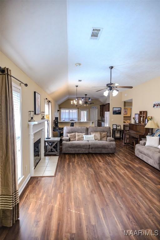 living room with vaulted ceiling, a tiled fireplace, wood finished floors, and visible vents