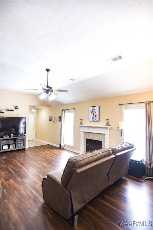 living area featuring visible vents, ceiling fan, wood finished floors, a tile fireplace, and baseboards