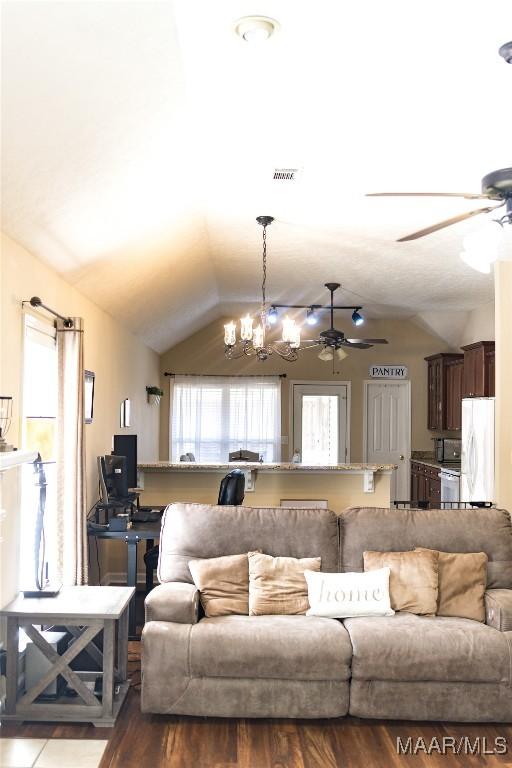 living area with visible vents, vaulted ceiling, and ceiling fan with notable chandelier