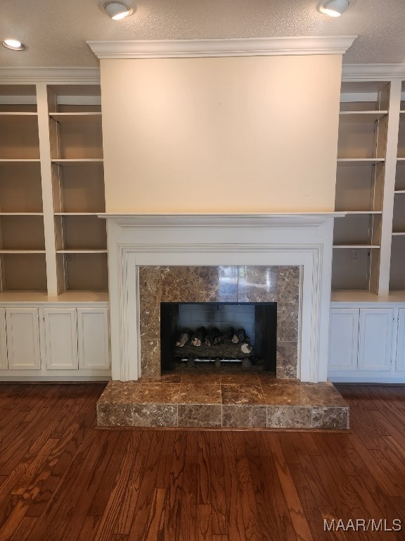 room details featuring a textured ceiling, a fireplace with raised hearth, crown molding, and wood finished floors