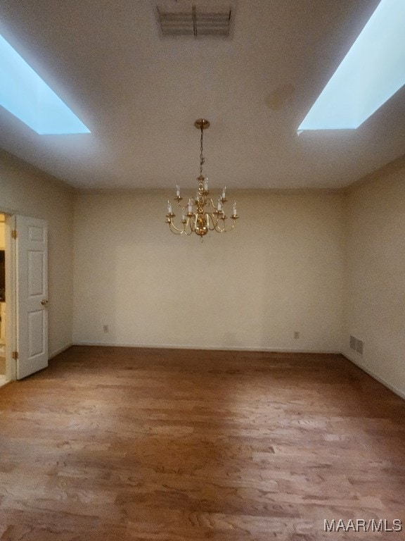 empty room featuring a skylight, visible vents, and wood finished floors