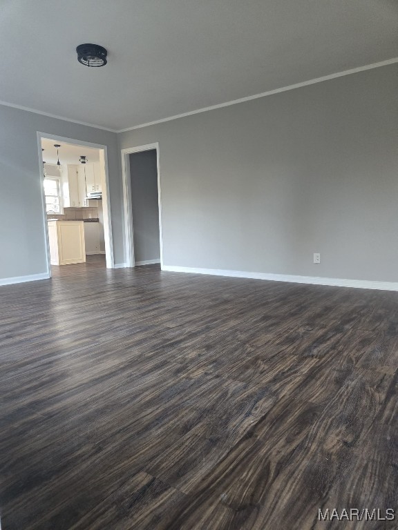 unfurnished living room featuring baseboards, dark wood finished floors, and crown molding