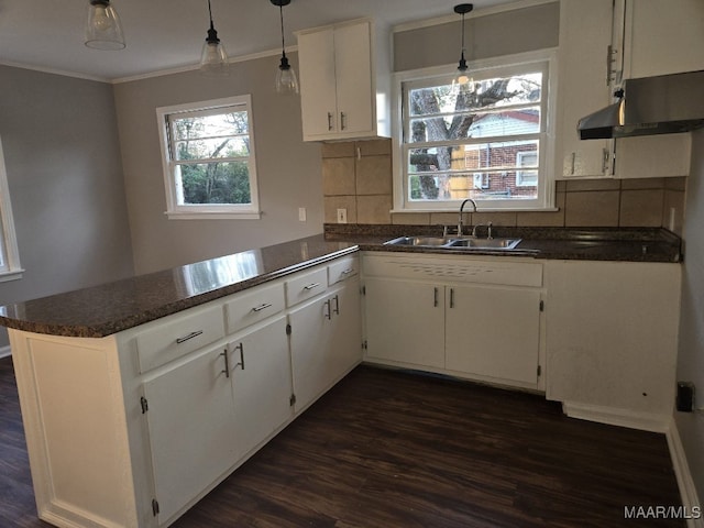 kitchen featuring white cabinets, dark countertops, a peninsula, crown molding, and a sink