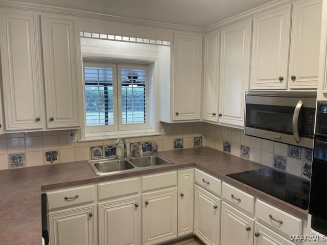 kitchen with stainless steel microwave, a sink, black electric stovetop, and white cabinetry