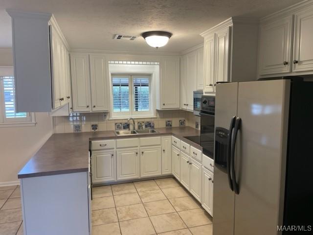 kitchen with dark countertops, a sink, refrigerator with ice dispenser, and light tile patterned floors