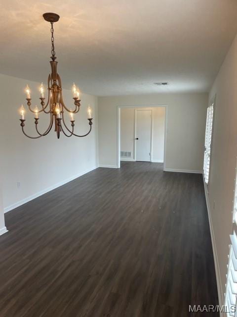 spare room featuring a notable chandelier, baseboards, and dark wood-type flooring