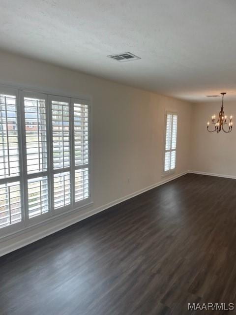 spare room with baseboards, dark wood-type flooring, visible vents, and a notable chandelier