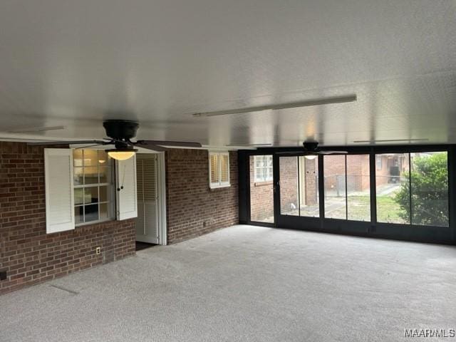 carpeted spare room with ceiling fan and brick wall