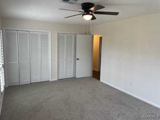 unfurnished bedroom featuring visible vents, baseboards, a ceiling fan, multiple closets, and carpet