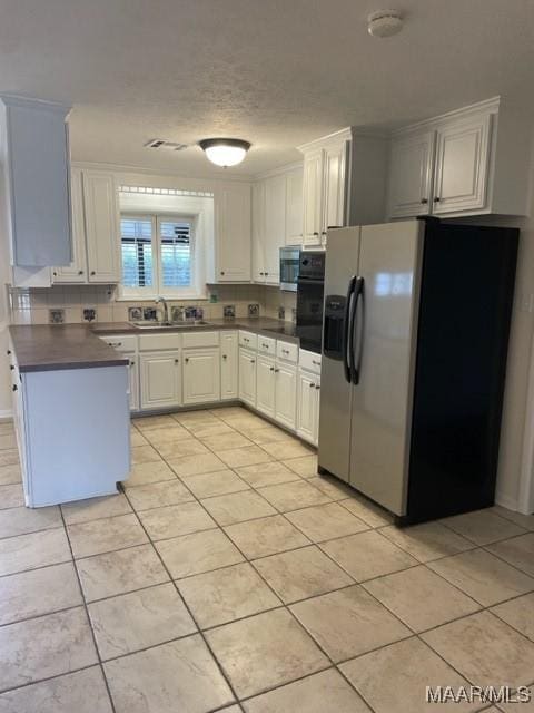 kitchen featuring light tile patterned flooring, stainless steel appliances, a sink, white cabinets, and dark countertops