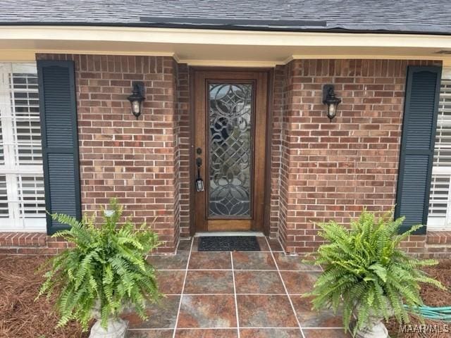 property entrance featuring brick siding and a shingled roof