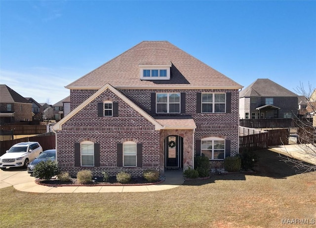 traditional-style house featuring brick siding, a front yard, fence, and a shingled roof