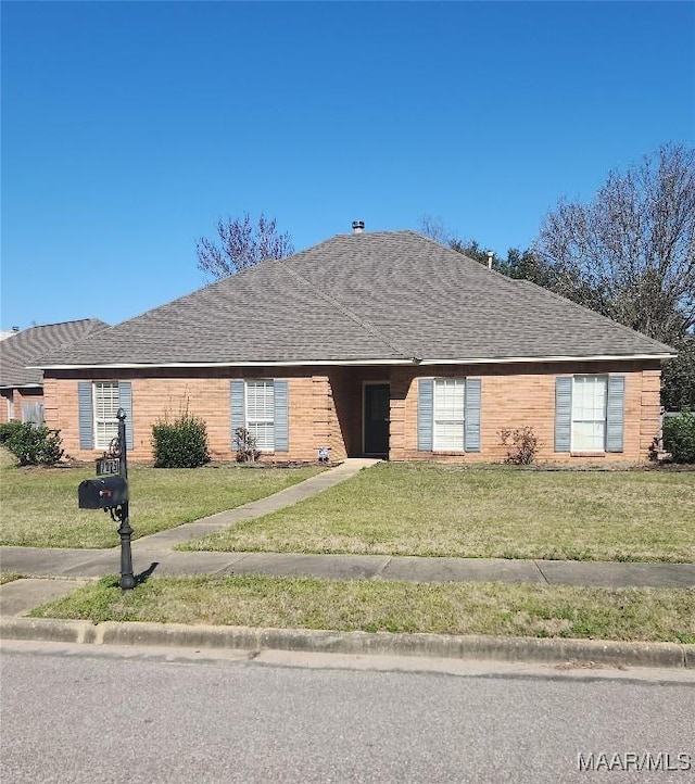 ranch-style home with a front lawn, roof with shingles, and brick siding