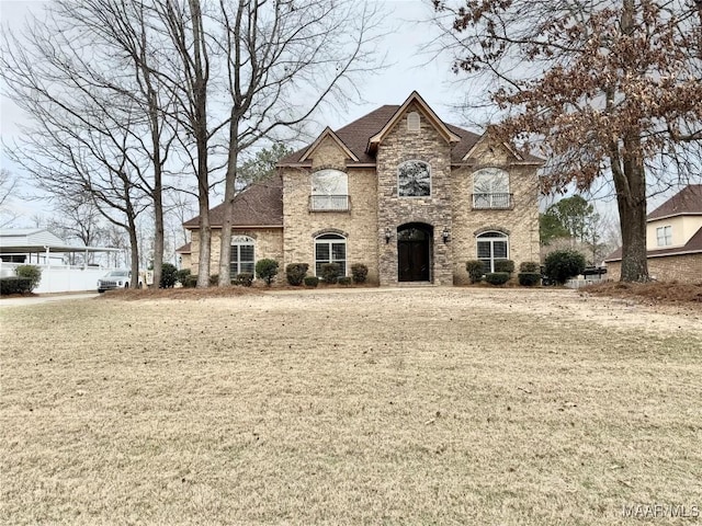 french country style house featuring stone siding, brick siding, a front lawn, and roof with shingles