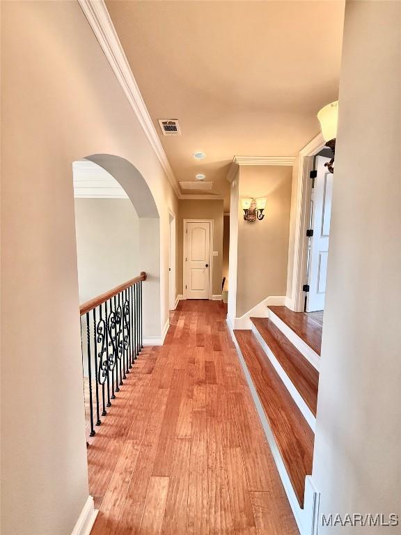 hallway with crown molding, visible vents, baseboards, and wood finished floors