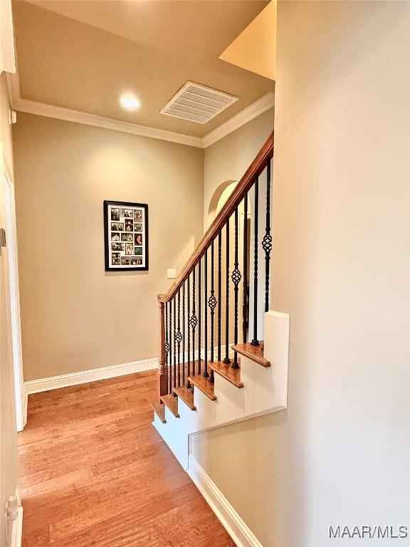 staircase with baseboards, visible vents, wood finished floors, and ornamental molding