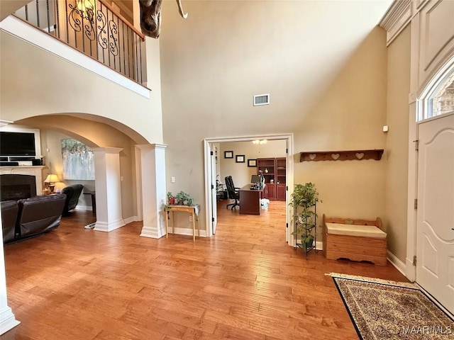 entryway with a tile fireplace, light wood-style flooring, visible vents, baseboards, and ornate columns