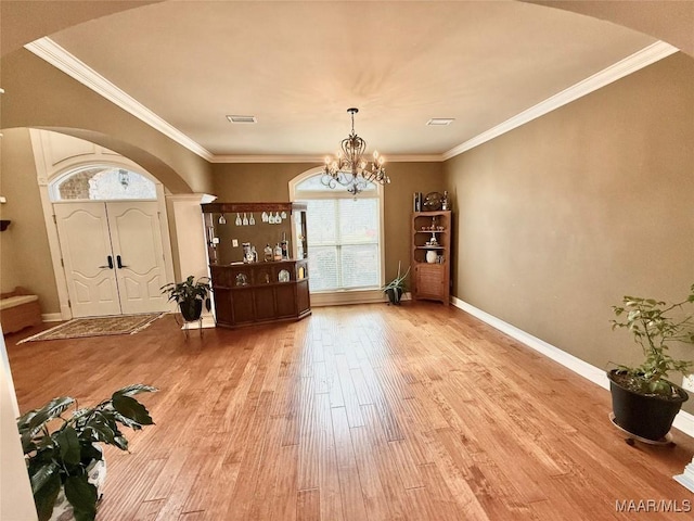 foyer entrance with visible vents, arched walkways, ornamental molding, wood finished floors, and a notable chandelier