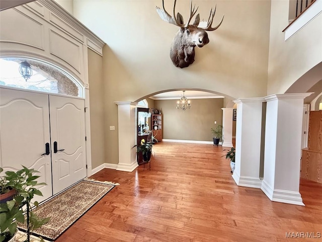 foyer with arched walkways, ornate columns, light wood-style flooring, a towering ceiling, and baseboards