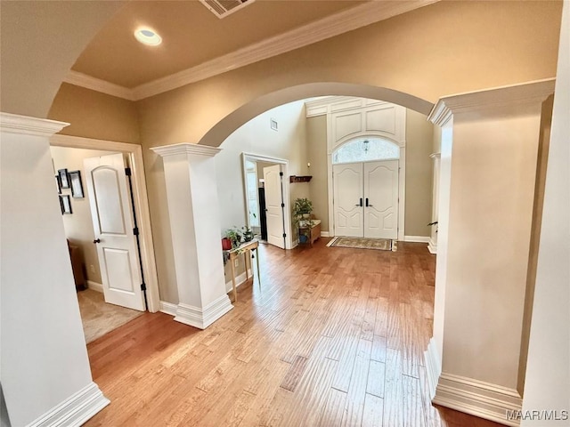 entrance foyer featuring arched walkways, ornamental molding, light wood-type flooring, and baseboards