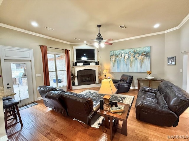 living area featuring light wood finished floors, a fireplace, visible vents, and ornamental molding