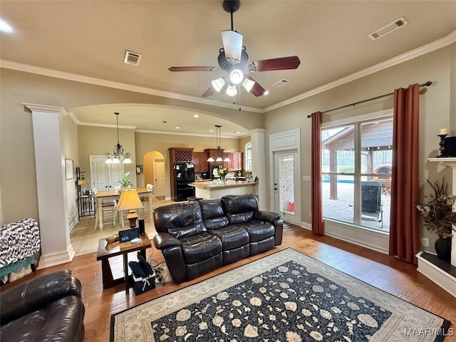 living area featuring arched walkways, ceiling fan with notable chandelier, visible vents, and light wood-style floors