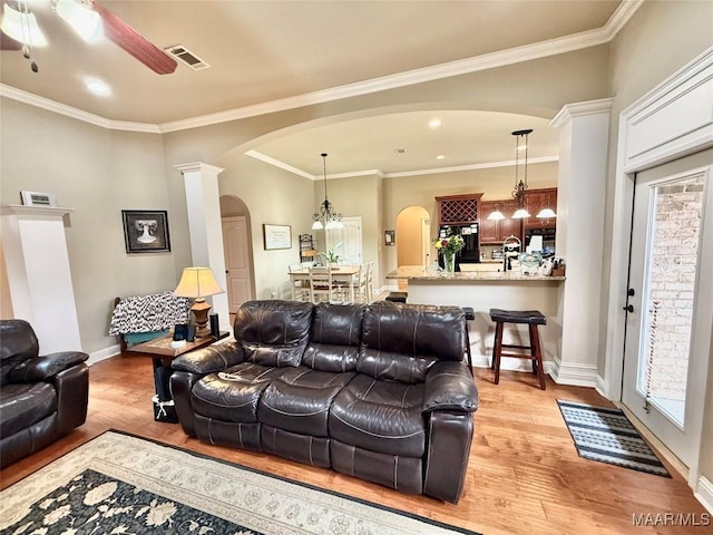 living area featuring arched walkways, light wood-type flooring, baseboards, and crown molding