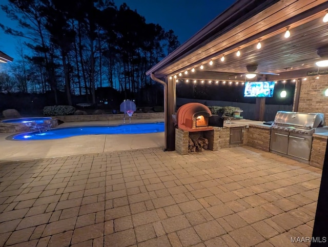 patio at night featuring an outdoor pool, a grill, an outdoor kitchen, and an in ground hot tub