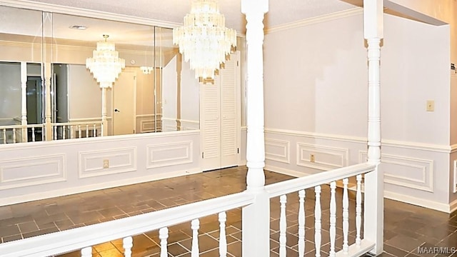 interior space featuring an inviting chandelier, ornamental molding, a decorative wall, and wainscoting