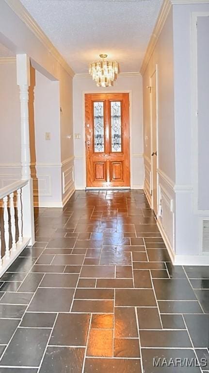 entrance foyer featuring a textured ceiling, ornamental molding, a decorative wall, and a notable chandelier