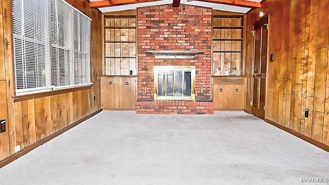 unfurnished living room featuring built in features, lofted ceiling with beams, carpet floors, wood walls, and a fireplace