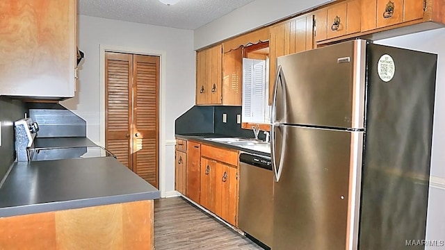 kitchen featuring stainless steel appliances, light wood-style floors, brown cabinetry, a sink, and a textured ceiling