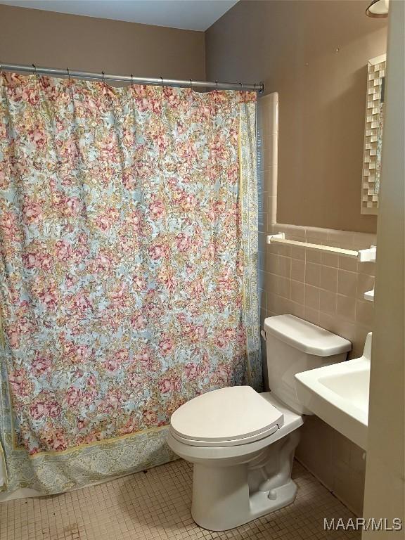 full bath with toilet, a shower with curtain, tile walls, and tile patterned floors