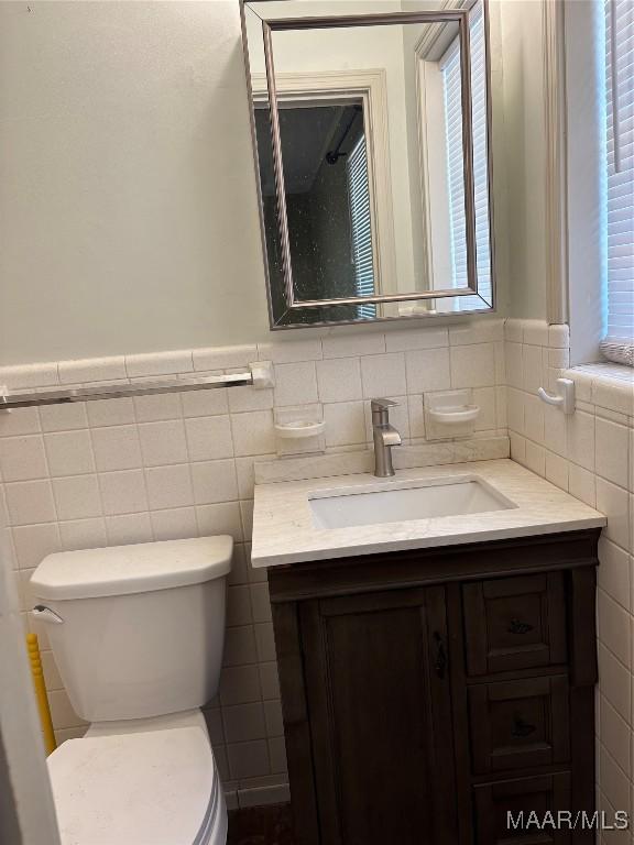 bathroom with wainscoting, vanity, toilet, and tile walls