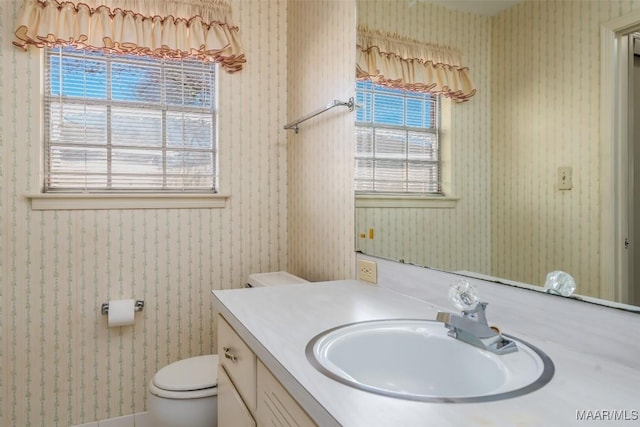 bathroom featuring toilet, plenty of natural light, vanity, and wallpapered walls