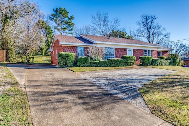 ranch-style house featuring driveway, fence, a front lawn, and brick siding