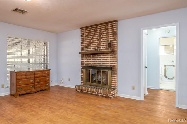 unfurnished living room featuring a brick fireplace, visible vents, baseboards, and wood finished floors