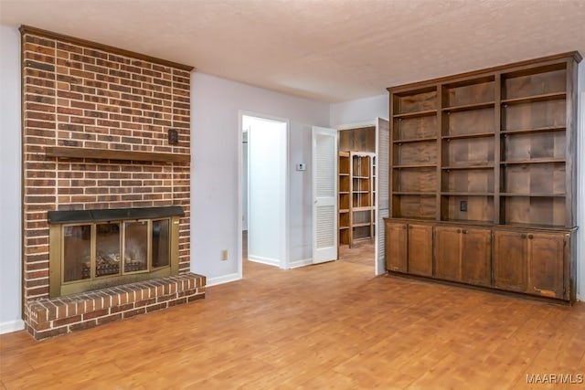 unfurnished living room with a brick fireplace, wood finished floors, and baseboards