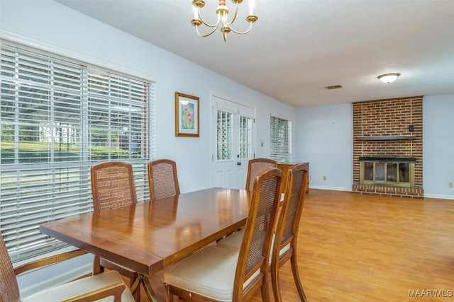 dining space featuring a brick fireplace, light wood-style flooring, baseboards, and an inviting chandelier