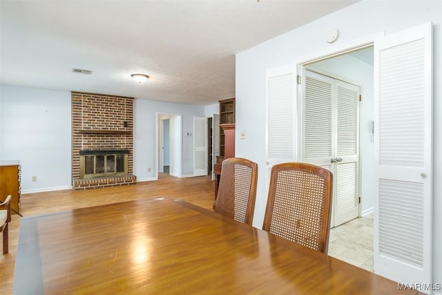 living area featuring a brick fireplace, visible vents, baseboards, and wood finished floors