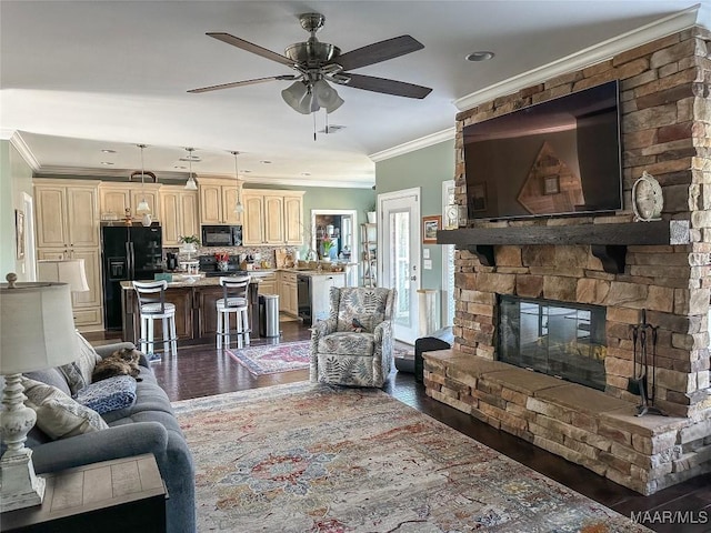 living room with dark wood-style floors, a stone fireplace, a ceiling fan, and crown molding