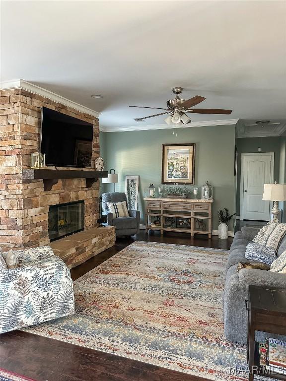 living room featuring a ceiling fan, a stone fireplace, crown molding, and wood finished floors